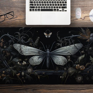 May include: A black and white illustration of a moth with large wings, surrounded by black and white floral details. The moth is centred in the image and has a dark body with white wings.