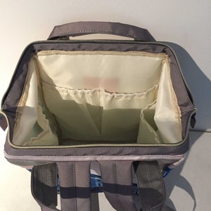 K&ouml;nnte beinhalten: Ein grauer Rucksack mit mehreren Taschen und F&auml;chern. Der Rucksack hat einen Rei&szlig;verschluss und verstellbare Tr&auml;ger.