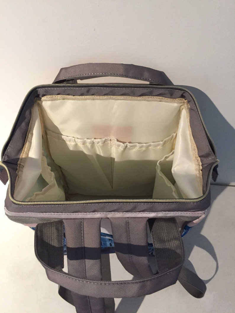 K&ouml;nnte beinhalten: Ein grauer Rucksack mit mehreren Taschen und F&auml;chern. Der Rucksack hat einen Rei&szlig;verschluss und verstellbare Tr&auml;ger.