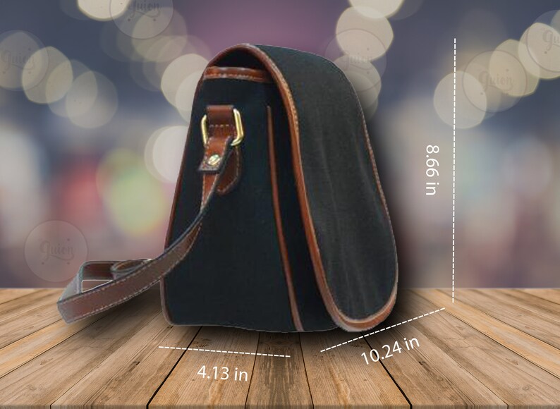 Puede incluir: Un bolso de hombro de lona negra con ribetes de cuero marr&oacute;n y una hebilla dorada. El bolso mide 10,24 pulgadas de ancho, 8,66 pulgadas de alto y 4,13 pulgadas de profundidad.