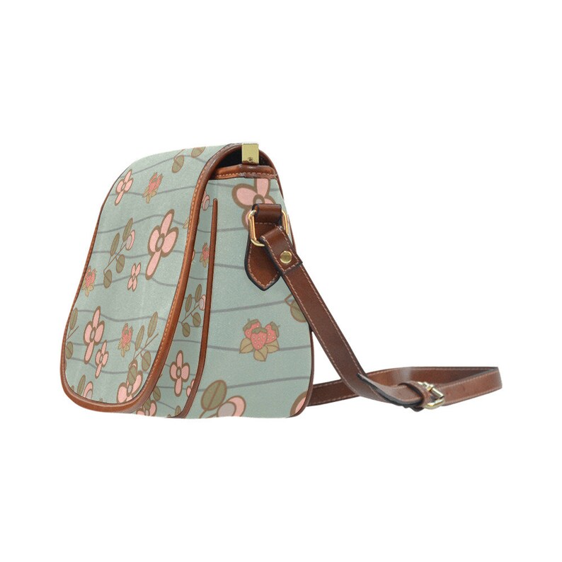 May include: A light blue crossbody bag with a floral pattern. The bag features pink flowers and brown accents, including the strap and trim. The bag has a gold-colored clasp.