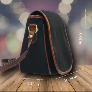 May include: A black canvas shoulder bag with brown leather trim and a gold buckle. The bag measures 10.24 inches wide, 8.66 inches tall, and 4.13 inches deep.