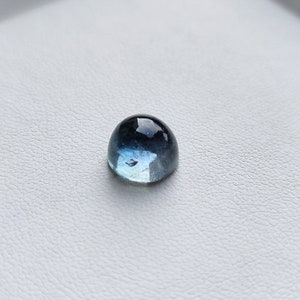 May include: A cabochon gemstone with a rounded top, displaying a gradient of colors from deep blue to light blue. The polished surface reflects light, creating a glossy appearance. The gemstone is set against a white background.