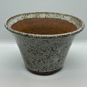 May include: A ceramic bowl with a speckled gray and white exterior and a brown interior. The rim is white with a textured edge. The bowl has a flared shape and a dark brown base.