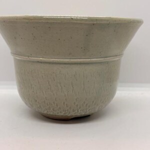 May include: A light gray ceramic planter with a textured surface. The planter has a wide, flared rim and a rounded base. The exterior features a subtle, speckled pattern, adding visual interest to the design.