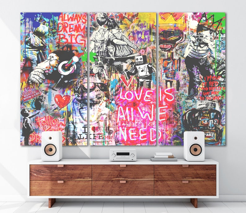May include: A colourful triptych canvas print with a graffiti style design. The centre panel features the words "Love is all we need" in pink and white lettering. The left panel features a figure wearing a red heart and the right panel features a figure holding a camera.