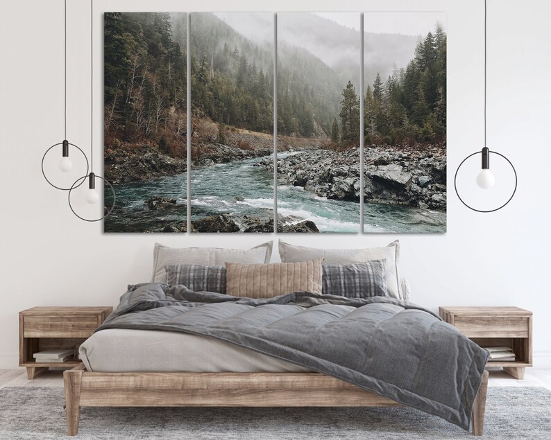 May include: A three-panel canvas print featuring a misty forest scene with a river flowing through it. The river is a vibrant blue-green color and the forest is a dark green. The canvas is mounted on a wooden frame and is hanging above a bed with gray bedding.