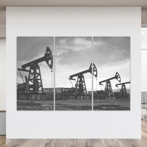 May include: A black and white photo of three oil derricks pumping oil in a field. The sky is cloudy and the ground is dry.