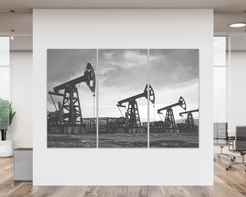 May include: A black and white photo of three oil derricks pumping oil in a field. The sky is cloudy and the ground is dry.