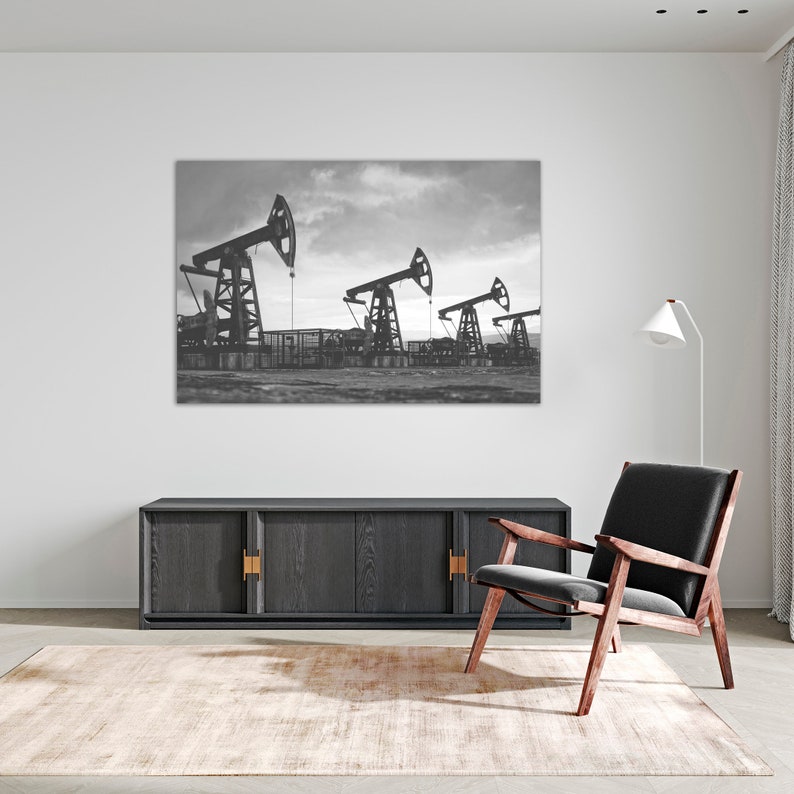 May include: Black and white photograph of three oil derricks in a field. The derricks are silhouetted against a cloudy sky.
