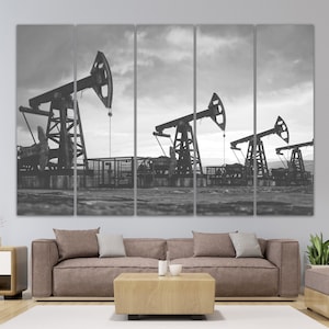 May include: Black and white photograph of three oil derricks pumping oil in a field. The derricks are silhouetted against a cloudy sky.