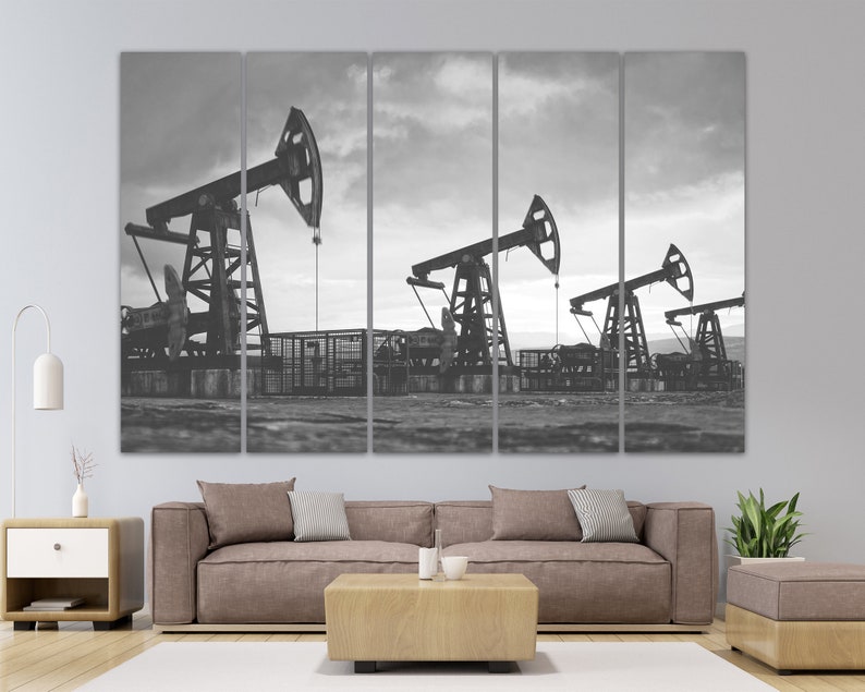 May include: Black and white photograph of three oil derricks pumping oil in a field. The derricks are silhouetted against a cloudy sky.