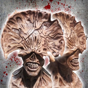 May include: A close-up of a detailed, hand-painted, brown and beige monster mask with a large, open mouth and sharp teeth. The mask has a textured, fleshy appearance and is reminiscent of a creature from a horror movie.