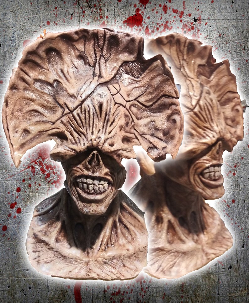 May include: A close-up of a detailed, hand-painted, brown and beige monster mask with a large, open mouth and sharp teeth. The mask has a textured, fleshy appearance and is reminiscent of a creature from a horror movie.