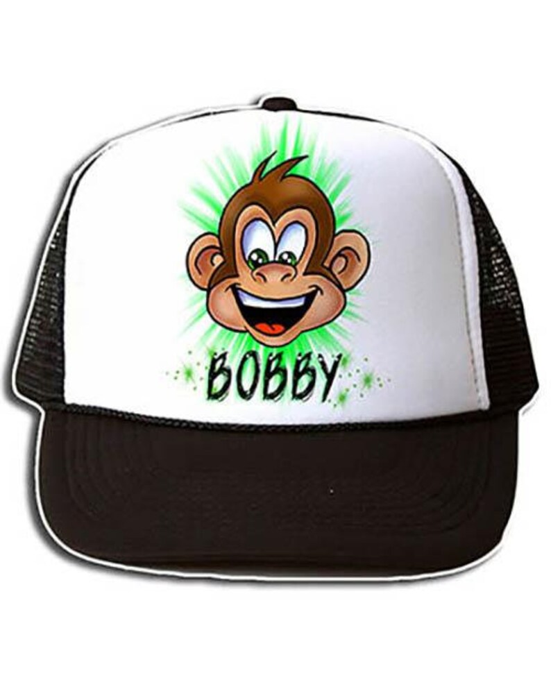 May include: A white and black trucker hat with a green and white cartoon monkey face and the name "BOBBY" printed on the front.