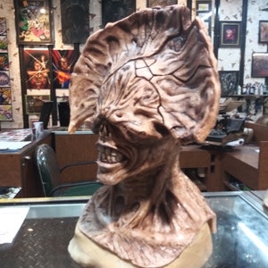 May include: A detailed, brown and beige, sculpted bust of a creature with a large, textured head and a gaping mouth.