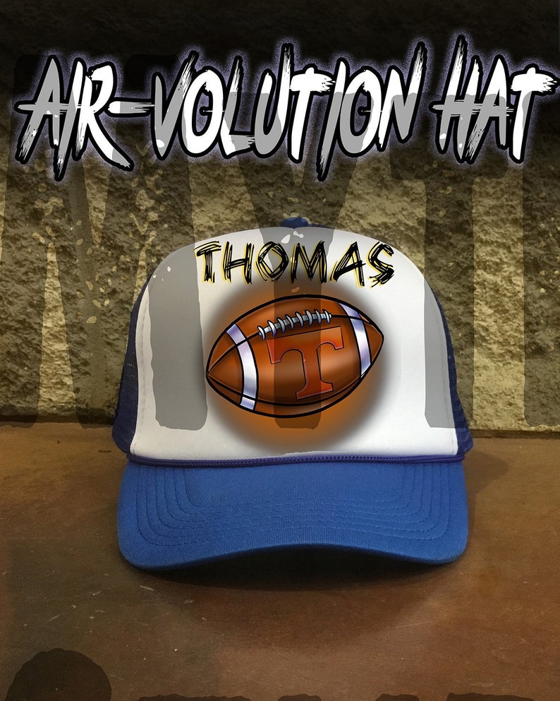 May include: A white and blue trucker hat with a blue brim. The hat has a white mesh back and a white front panel with a brown football and the name "THOMAS" printed in black.