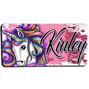 May include: A pink and white personalized license plate featuring a colorful unicorn with a rainbow mane and tail. The name "Kinley" is written in black cursive lettering.