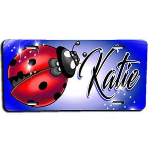 May include: A blue and white personalized license plate with a red and black ladybug design. The name "Katie" is written in a decorative font.