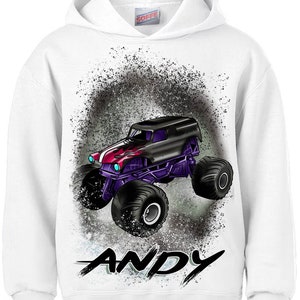 May include: White hooded sweatshirt with a black and purple monster truck graphic and the name "ANDY" printed in black below the truck. The truck is set against a gray and green splatter background.