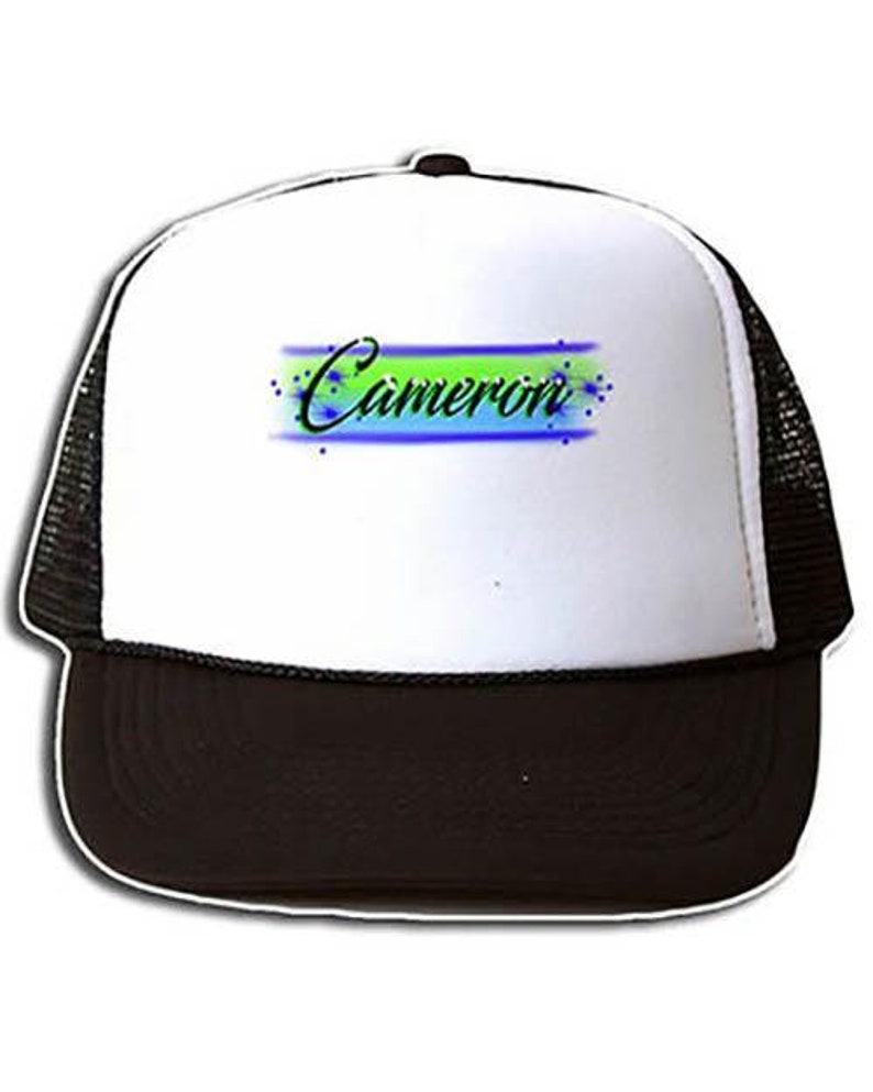 May include: A white trucker hat with a black mesh back. The front of the hat has a green, blue, and white design with the name "Cameron" written in black.