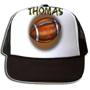 May include: A white and black trucker hat with a black mesh back. The front of the hat features a brown football with a white 'T' and the name 'THOMAS' in yellow lettering.