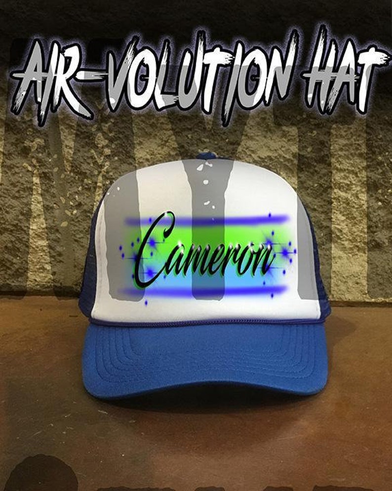 May include: A blue and white trucker hat with a mesh back. The hat has a green and blue airbrushed design with the name "Cameron" written in black.