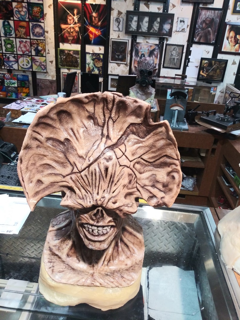 May include: A detailed, hand-painted, brown and beige sculpture of a creature with a large, open mouth and a single eye. The sculpture is displayed on a glass surface.