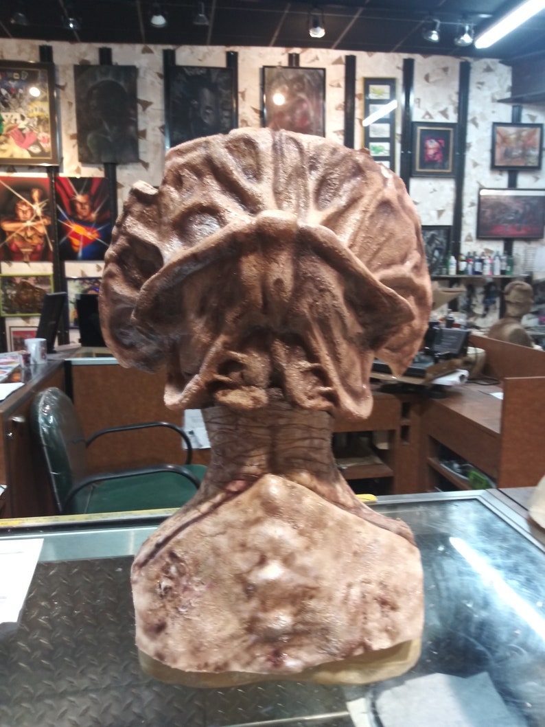 May include: A brown and beige detailed bust sculpture of a creature with a large head and a textured surface.