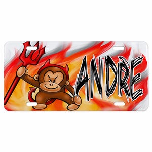 May include: A rectangular license plate featuring a cartoon monkey with red devil horns and a tail, holding a red trident. The background displays vibrant orange and red flames. The name ANDRE is printed in large, black, stylized lettering.
