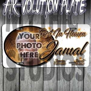 May include: A white memorial license plate with a gold circle containing a photo placeholder and the text "YOUR PHOTO HERE". The text "Rest In Heaven Jamal" is in gold lettering with a gold gate design. The dates "Sunrise 1-20-1990 Sunset 26-2001" are in gold lettering.