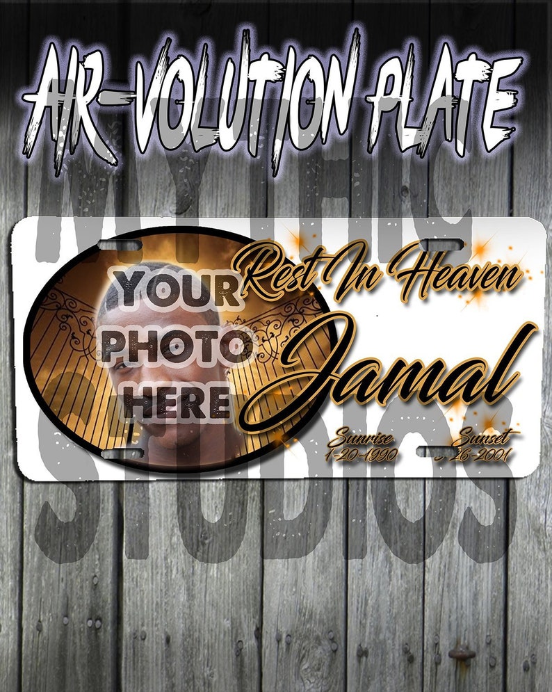 May include: A white memorial license plate with a gold circle containing a photo placeholder and the text "YOUR PHOTO HERE". The text "Rest In Heaven Jamal" is in gold lettering with a gold gate design. The dates "Sunrise 1-20-1990 Sunset 26-2001" are in gold lettering.