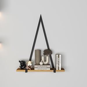May include: A black metal triangular shelf with a wooden shelf, holding a small black and white figurine, a small white figurine, a gray vase, a brown vase, and a stack of books with the titles "OLD MAN AND THE SEA", "HENRI MATISSE", "DESIGN BY NATURE", "THE ART OF", and "BODY OF ART".