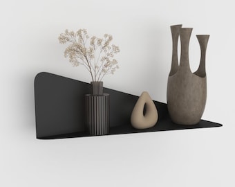 May include: A black metal shelf with a curved edge, featuring a vase with dried flowers, a small brown ceramic sculpture, and a brown ceramic vase with three openings.