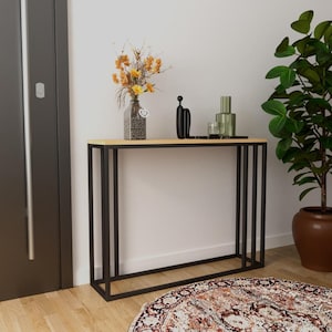 Könnte beinhalten: Ein moderner Konsolentisch mit einer hellen Holzplatte und einem schwarzen Metallrahmen. Der Tisch ist mit einer Vase mit gelben Blumen, einer schwarzen Skulptur und grünen Glasflaschen dekoriert. Eine Topfpflanze und ein gemusterter Teppich sind ebenfalls zu sehen.