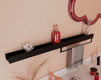 May include: A black metal bathroom shelf with a built-in towel bar. The shelf holds a red soap dispenser, cotton swabs, and a gray towel. A decorative mirror is visible in the background.