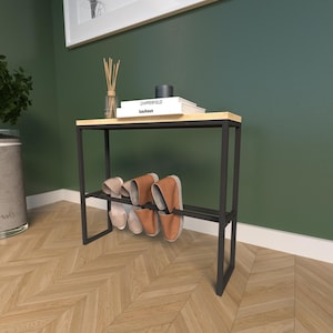 May include: A black metal shoe rack with a light wood top and a lower shelf. Several pairs of slippers in shades of tan and brown are displayed on the rack. The top shelf holds books and decorative items.