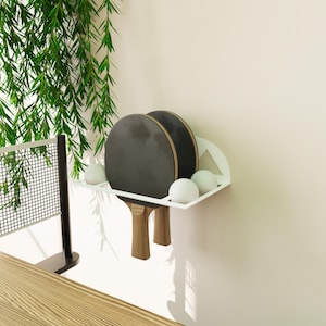 Minimalist table tennis paddle and ball holder, black metal wall shelf with geometric Squid Game-inspired design for gamers and fans