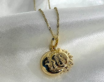 May include: A gold-colored necklace with a pendant featuring a sun and moon design. The pendant is round with detailed carvings of the sun and moon. The necklace chain is a delicate, twisted rope style.