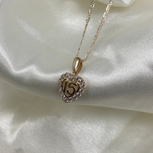 May include: Gold necklace with a heart-shaped pendant featuring the number 15 surrounded by clear cubic zirconia stones.