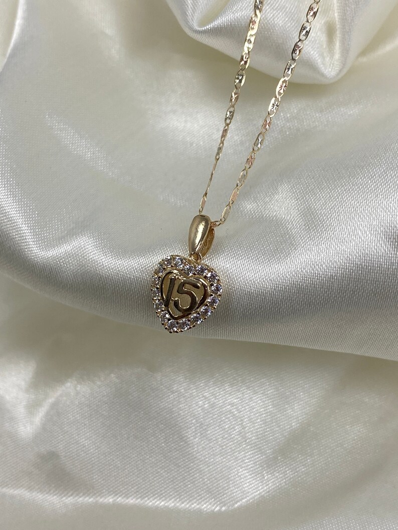 May include: Gold necklace with a heart-shaped pendant featuring the number 15 surrounded by clear cubic zirconia stones.