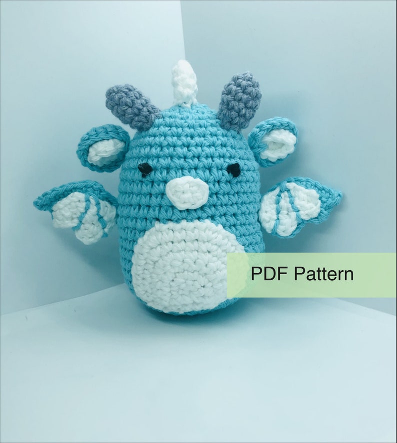 May include: A handmade crochet creature in shades of blue, white, and grey. The amigurumi has a round body, wings, and horns. The text "PDF Pattern" is visible on the image.