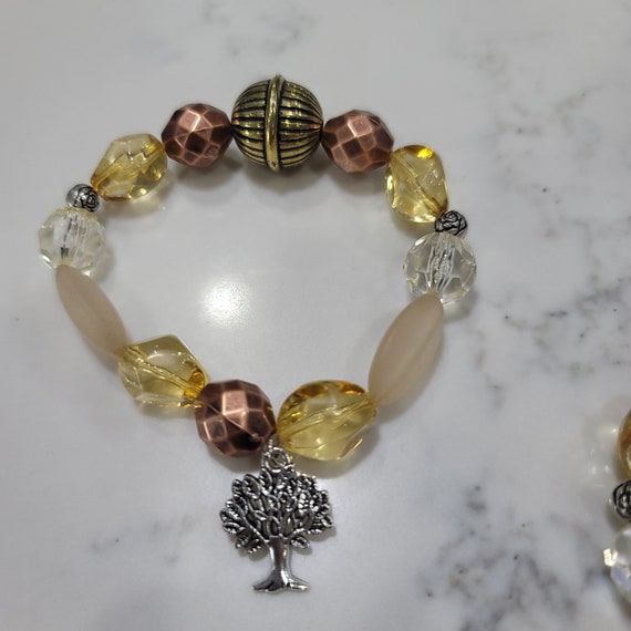 Honey colored stretch beaded bracelet. Warm appeal with copper and honey colors separated by rose spacers with Tree of Life dangle charm