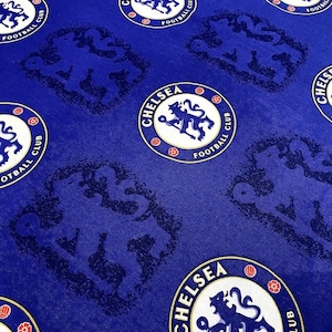 May include: Close-up of a blue fabric featuring the Chelsea Football Club logo and a repeating pattern of the club's emblem. The logo is a white circle with the words "CHELSEA FOOTBALL CLUB" and a blue lion. The background is a solid blue.