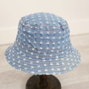 K&ouml;nnte beinhalten: Ein hellblauer Jeans-Bucket-Hut mit Used-Look. Der Hut hat eine breite Krempe und ein gen&auml;htes Design.