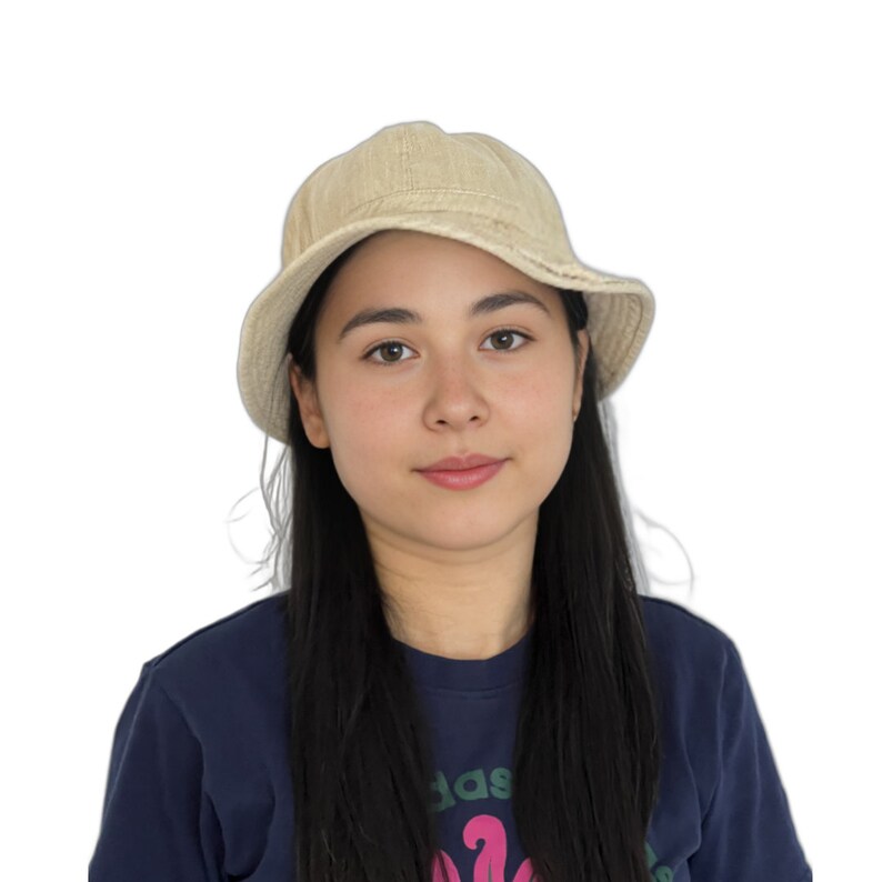 May include: A young person with long black hair wearing a beige bucket hat and a dark blue shirt with a graphic design.