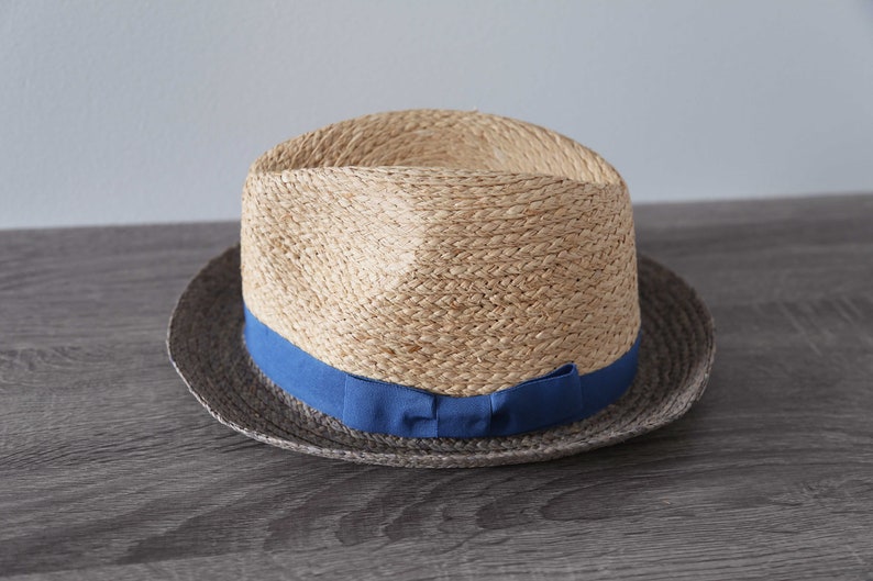 May include: A straw hat with a blue ribbon around the crown. The hat has a brown band around the brim.