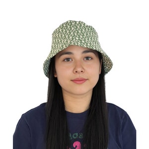 May include: A green bucket hat with a white floral pattern. The hat is worn by a person with long black hair.