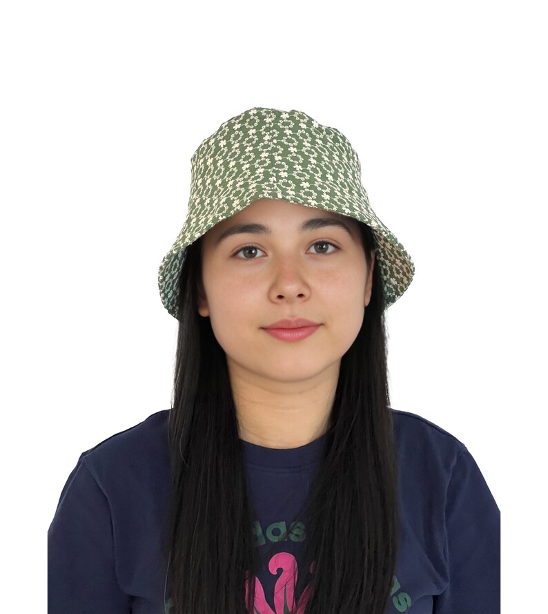 May include: A green bucket hat with a white floral pattern. The hat is worn by a person with long black hair.