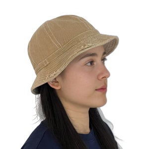 May include: A tan canvas bucket hat with a distressed brim. The hat is worn by a person with long black hair.
